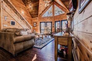 A cozy cabin interior with a wooden staircase, a sofa, a dining table, and a large window. - Owls and Friends - 3 King Bedroom with ensuites-Hot tub-Pool Table (Blue Ridge)