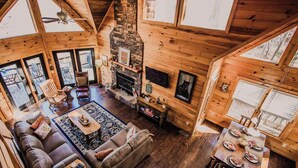 A spacious wooden cabin with a fireplace, a sofa, a dining table, and a TV mounted on the wall. - Owls and Friends - 3 King Bedroom with ensuites-Hot tub-Pool Table (Blue Ridge)