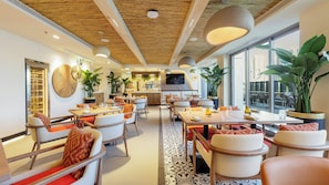 A modern restaurant with high ceilings, wooden beams, and large windows. Tables are set with chairs and centerpieces.