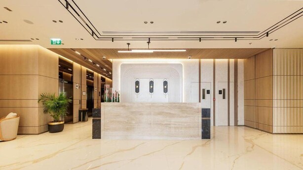 Een moderne hotellobby met een marmeren vloer, een receptiebalie en een grote plant.