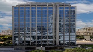 Een hoog gebouw met een moderne glazen gevel, meerdere verdiepingen en een centraal, verticaal element.