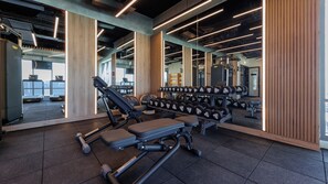Ein Fitnessraum mit Trainingsgeräten, Gewichtsständern und einem großen Spiegel, der den Raum widergibt.