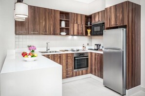 A modern kitchen with wooden cabinetry, a stainless steel refrigerator, and a white countertop. - Central Inn Hotel & Suites Al Sadd (Doha)
