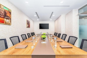 Un salón de conferencias con una larga mesa, sillas, un televisor de pantalla plana y un cuadro en la pared.