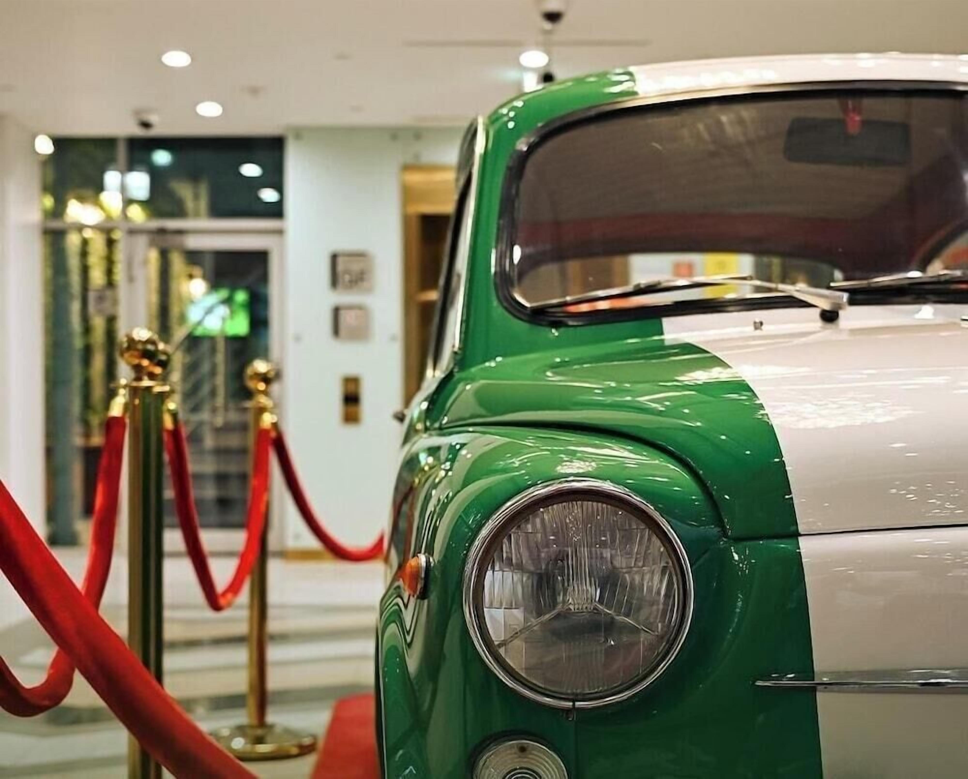 Un coche antiguo con una combinación de colores verde y blanco, estacionado en el interior con una barrera de cuerda roja.