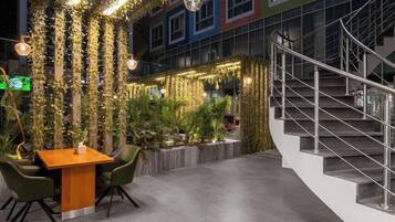 Un espacio interior con una escalera, una zona de comedor con mesa y sillas, y una pared cubierta de plantas y luces colgantes.