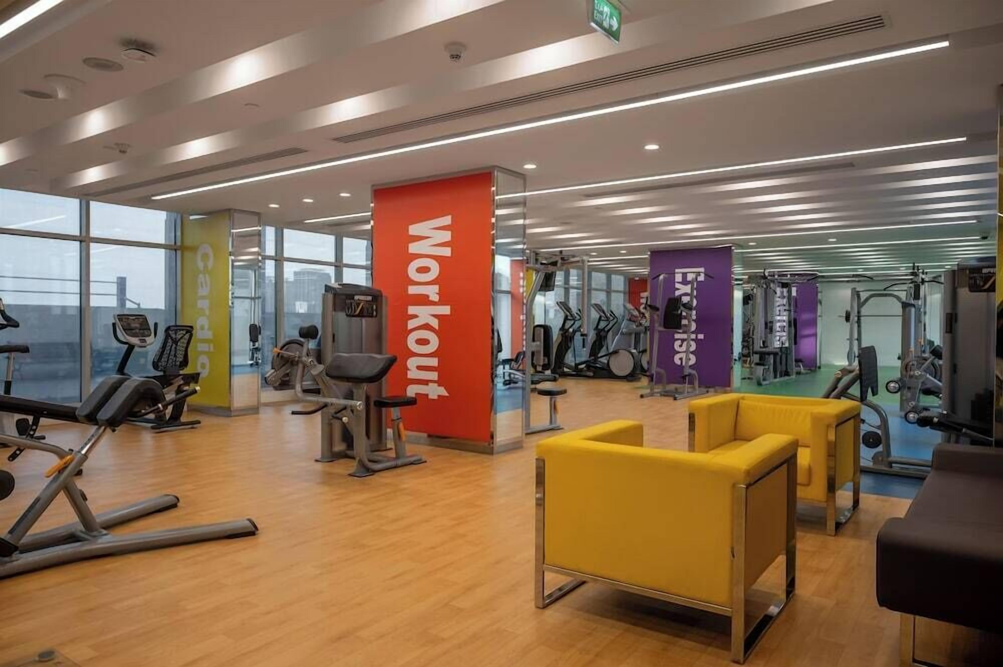 Un gimnasio con equipo de cardio y pesas, iluminación brillante y ventanas amplias.