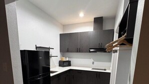 A modern kitchen with dark cabinetry, a black refrigerator, and a white countertop. - Studio6 Humble, TX (Humble)