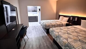 A hotel room with a desk, two beds with patterned bedding, a wardrobe, and a bathroom visible through an open door. - Studio6 Humble, TX (Humble)