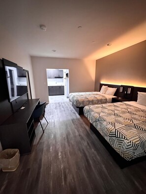 A hotel room with a desk, two beds with patterned bedding, a wardrobe, and a bathroom visible through an open door. - Studio6 Humble, TX (Humble)