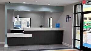 A reception area with a counter, a digital screen, and a window with a view of the outside. - Studio6 Humble, TX (Humble)