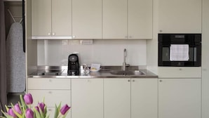 A modern kitchen with white cabinets, a coffee maker, a sink, and a built-in oven. - Waterfront Cabins (Gothenburg)