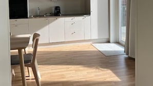 A compact kitchen with white cabinets, a dining table with chairs, and a large window providing natural light. - Waterfront Cabins (Gothenburg)