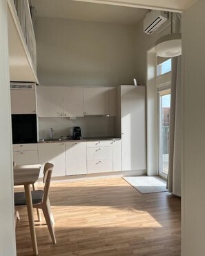 Una cocina compacta con armarios blancos, una mesa de comedor con sillas y un ventanal que proporciona luz natural.