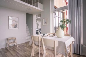 Un comedor con una mesa lista para dos comensales, una escalera y una ventana con cortinas.