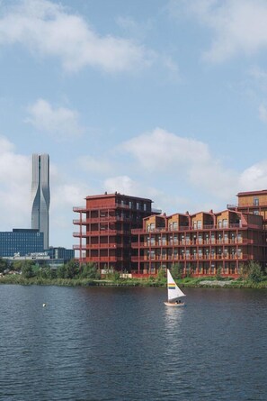 Un velero en aguas tranquilas, con edificios modernos al fondo.