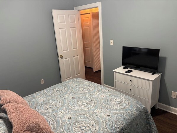 Un dormitorio con una cama, un televisor sobre una cómoda y una puerta que da a un armario.