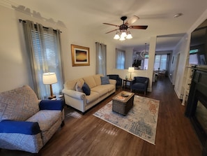 A living room with a sofa, armchair, coffee table, and a fireplace. - Center of the action - Family and Pet Friendly (Apex)