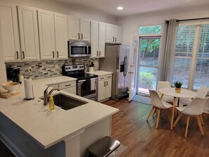 Una cocina moderna con armarios blancos, un refrigerador de acero inoxidable y un comedor con una mesa redonda y sillas.