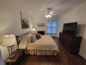A bedroom with a bed, a dresser, a television, a ceiling fan, and a window with blinds. - Center of the action - Family and Pet Friendly (Apex)