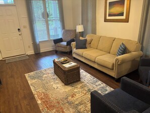 A living room with a beige sofa, a patterned rug, a small side table, and a chair. - Center of the action - Family and Pet Friendly (Apex)