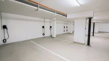 Eine saubere, leere Tiefgarage mit weißen Wänden und Böden, Neonbeleuchtung sowie sichtbaren Steckdosen an den Wänden.