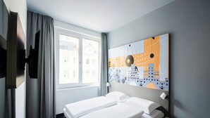 Hotelkamer met een bed, een raam met gordijnen, een tv aan de muur en een kunstwerk met een stadsgezicht.