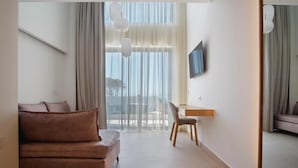 A modern hotel room with a sofa, a desk, and a large window with curtains. - Phos Hotel - Adults Only (Chania)