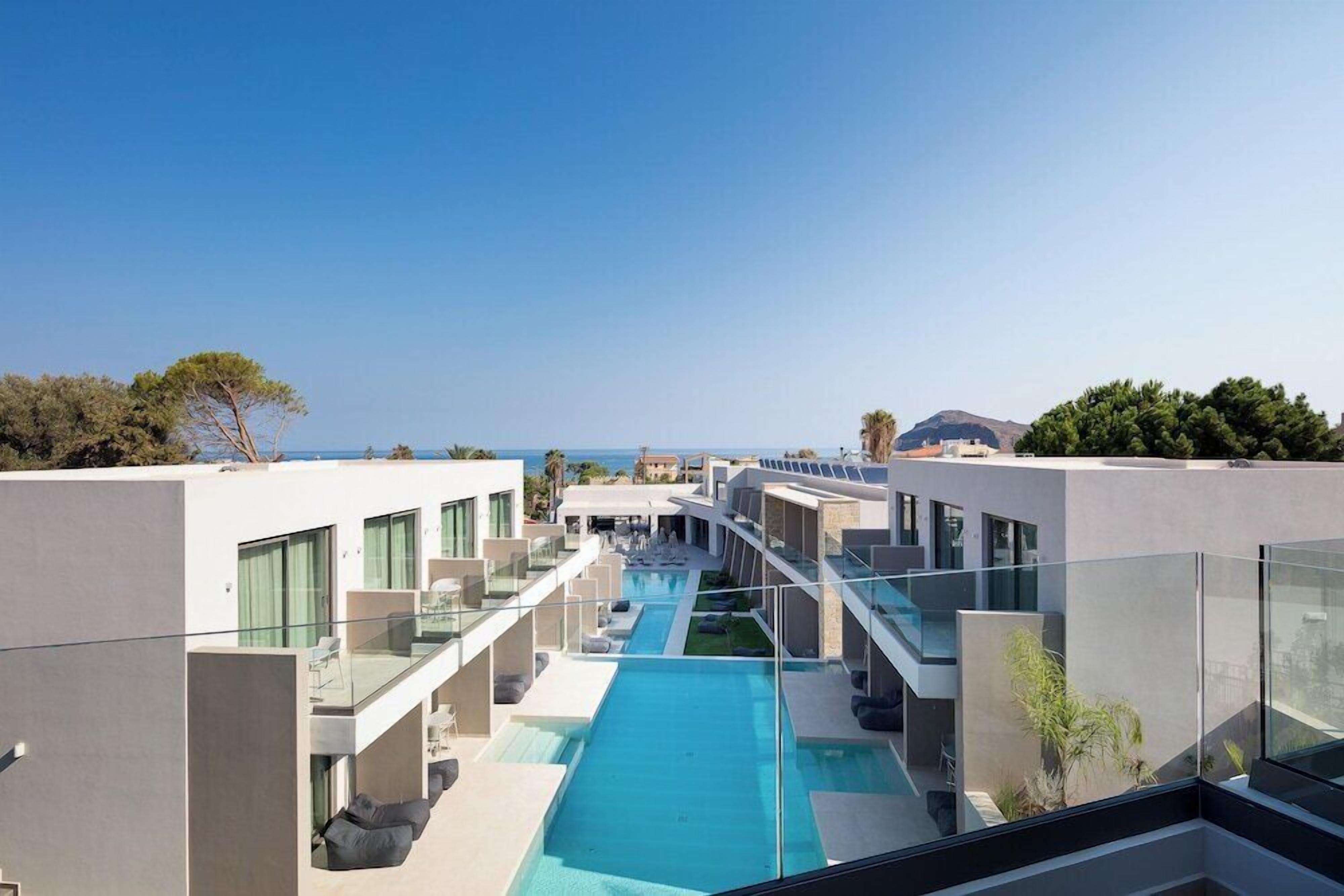Un hotel modern amb piscina al terrat, zones d'estar a l'aire lliure i vistes al mar.