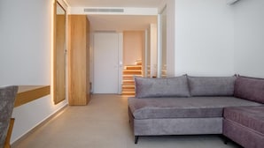 A modern living room with a grey sectional sofa, wooden flooring, and a staircase leading to an upper level. - Phos Hotel - Adults Only (Chania)
