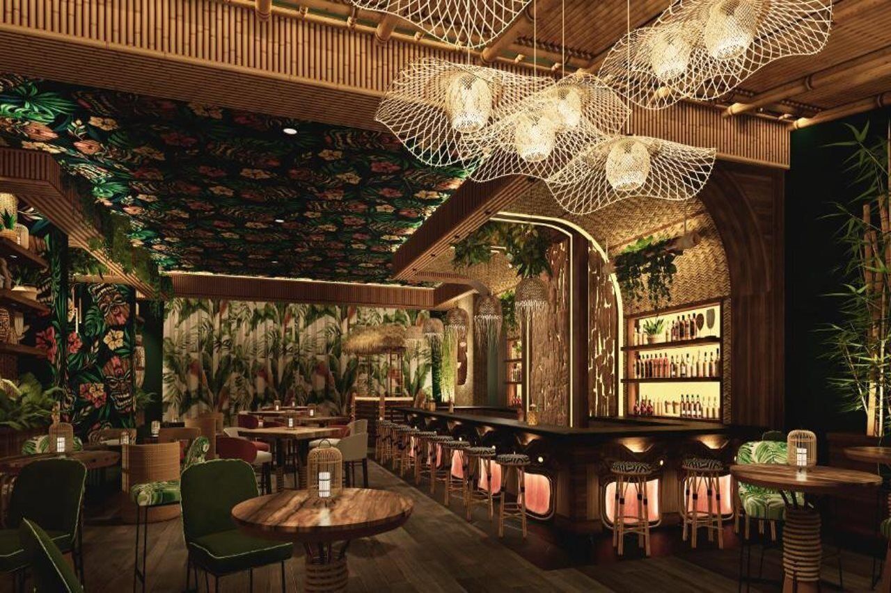 A bar area with wooden furniture, hanging lights, and a tropical-themed wall.