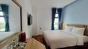 A hotel room with a bed, a TV, a window with curtains, and a table with a tray of items. - Haven Hut Riverside (Ho Chi Minh City)