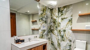 A modern bathroom with a marble shower wall, a white sink, and a toilet.