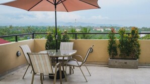A balcony with a table and chairs, an umbrella, and potted plants.