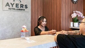 A reception desk with a logo for 'AYERS HOTEL & RESTO' and a clock on the wall.