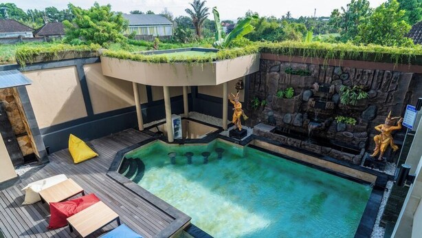 A rooftop swimming pool with a wooden deck, lounge chairs, and a stone wall with statues.