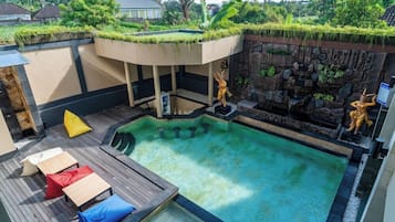 A rooftop swimming pool with a wooden deck, lounge chairs, and a stone wall with statues.