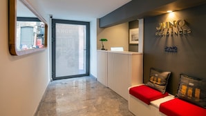 A reception area with a glass door, a reception desk, and a wall with the Juno Hotels logo. - Juno Residences (Istanbul)