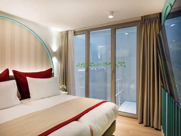 Hotellihuone, jossa on sänky, verhot ja näkymä lasiovesta.