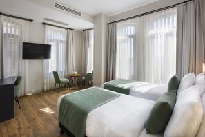 A hotel room with two beds, a desk, a television, and a small table with chairs. - Juno Residences (Istanbul)
