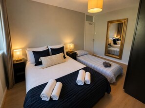 A hotel room with two beds, a large mirror, and a bedside lamp. - 1 Bdr Sleeps 4 1 Bath Holland Park (London)