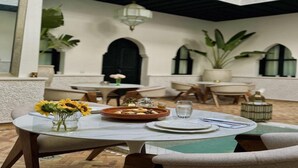 An outdoor dining area with a round table, chairs, a vase of sunflowers, and a water glass. - Riad El Khaeir Hammam & Spa (Marrakech)
