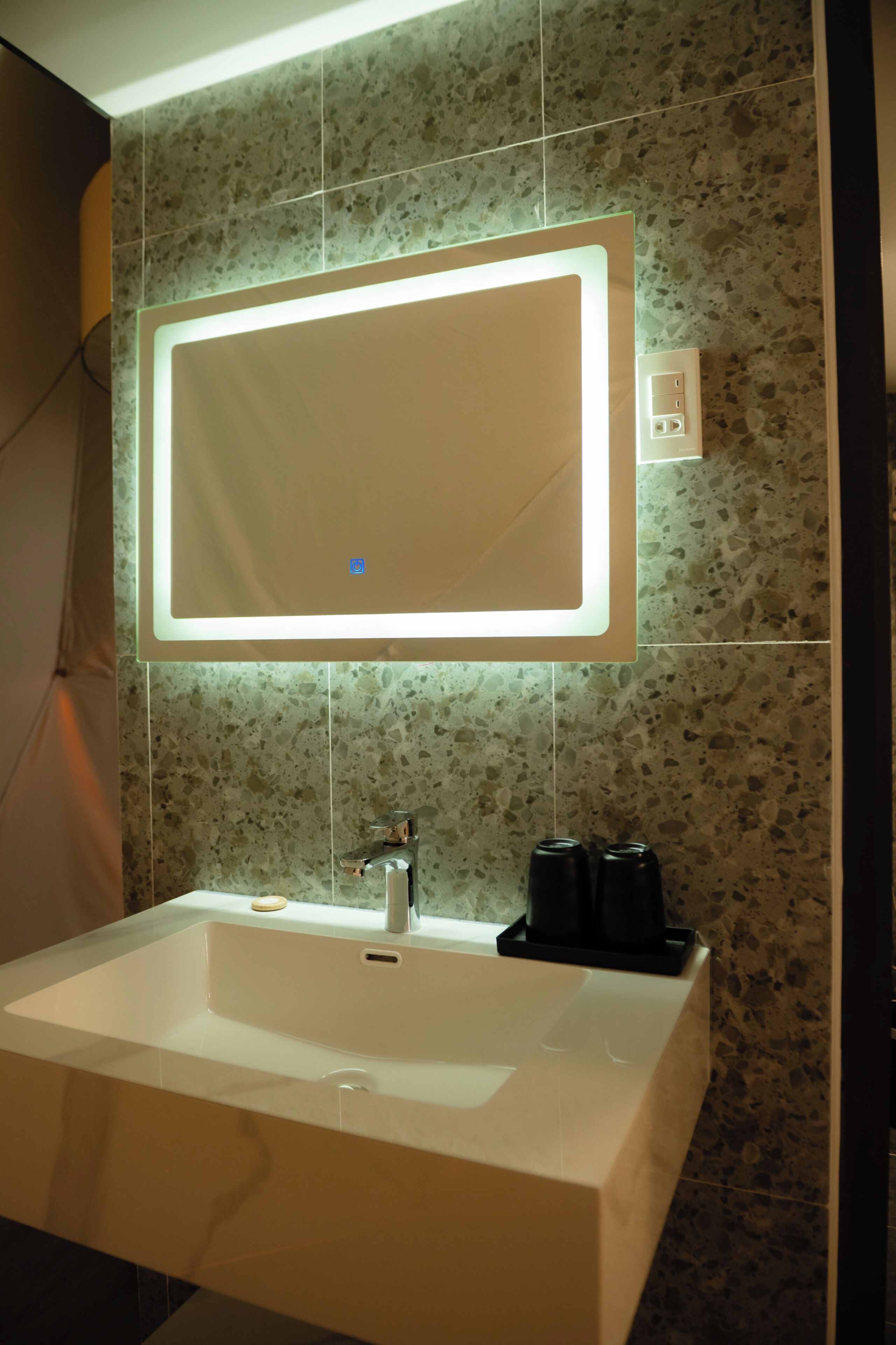 Ein Badezimmer mit einem rechteckigen Spiegel, einem weißen Waschbecken und einem Wasserhahn.