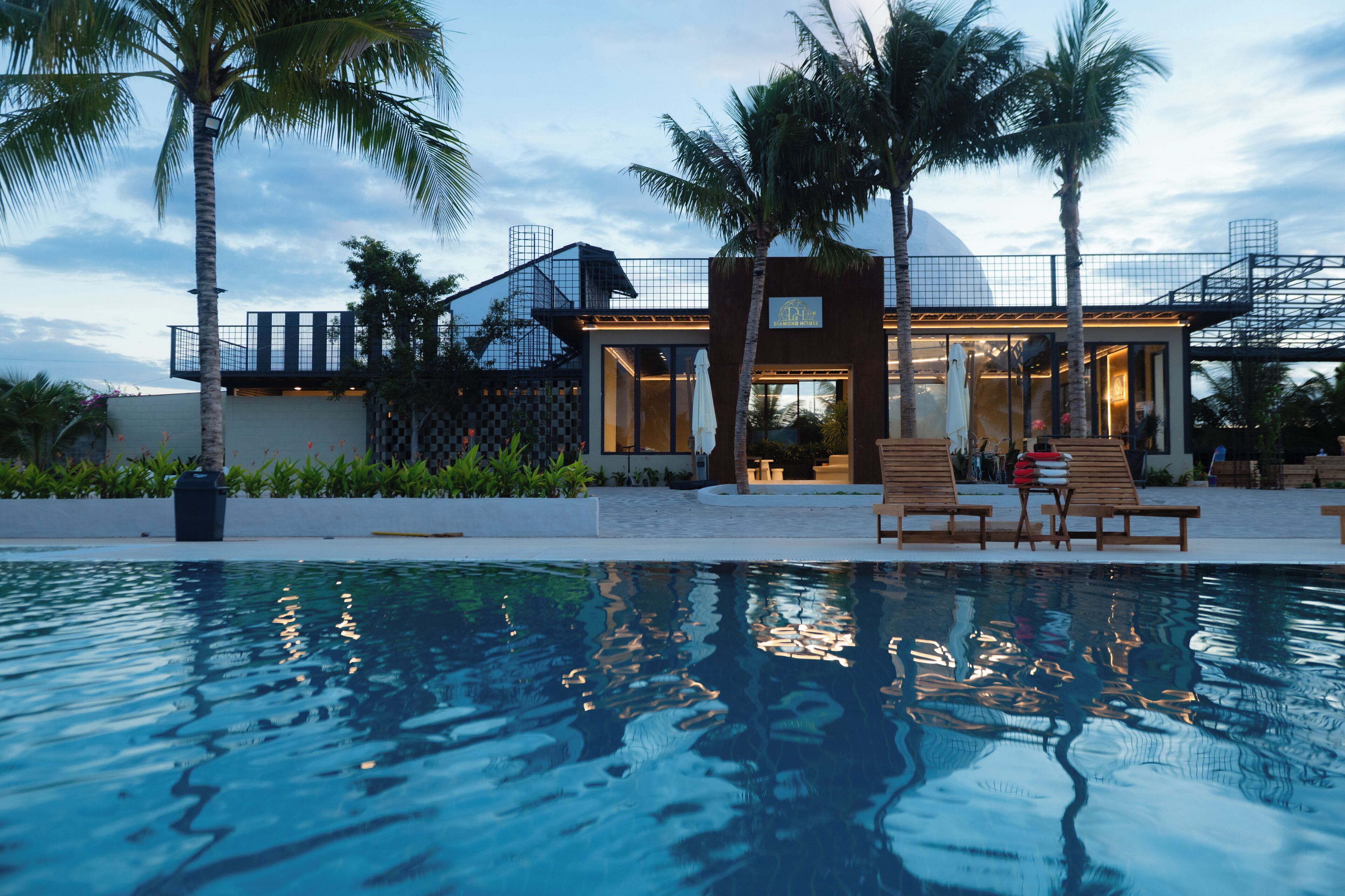A modern hotel with a pool, palm trees, and a clear sky.