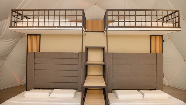 Une chambre avec un lit superposé, une étagère centrale, des têtes de lit en bois et du linge de lit blanc.