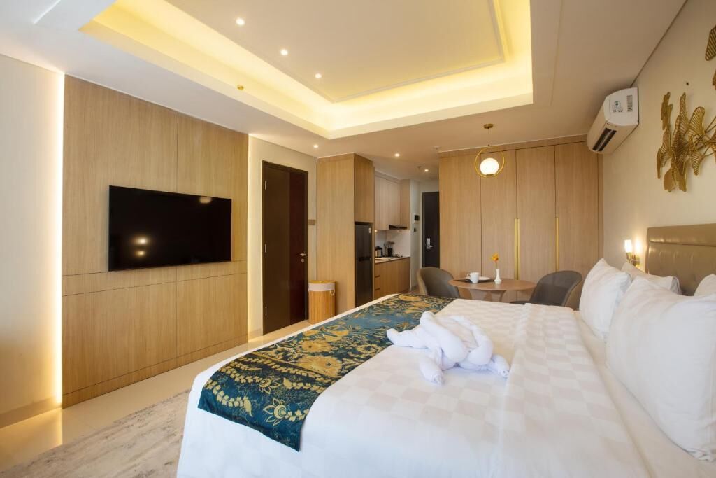 Une chambre d’hôtel avec un lit, un téléviseur à écran plat, un coin repas et une cuisine en arrière-plan.