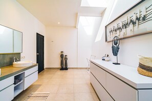 Uma casa de banho moderna com um espelho grande, uma pia e uma sanita. Há um porta-toalhas e uma peça decorativa na parede.