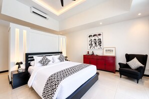 Une chambre à coucher moderne avec un grand lit, une commode rouge, un fauteuil noir et des œuvres d’art accrochées aux murs.
