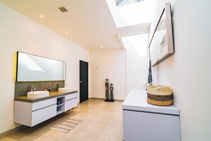 Une salle de bain moderne avec deux lavabos, un grand miroir et une fenêtre de toit.