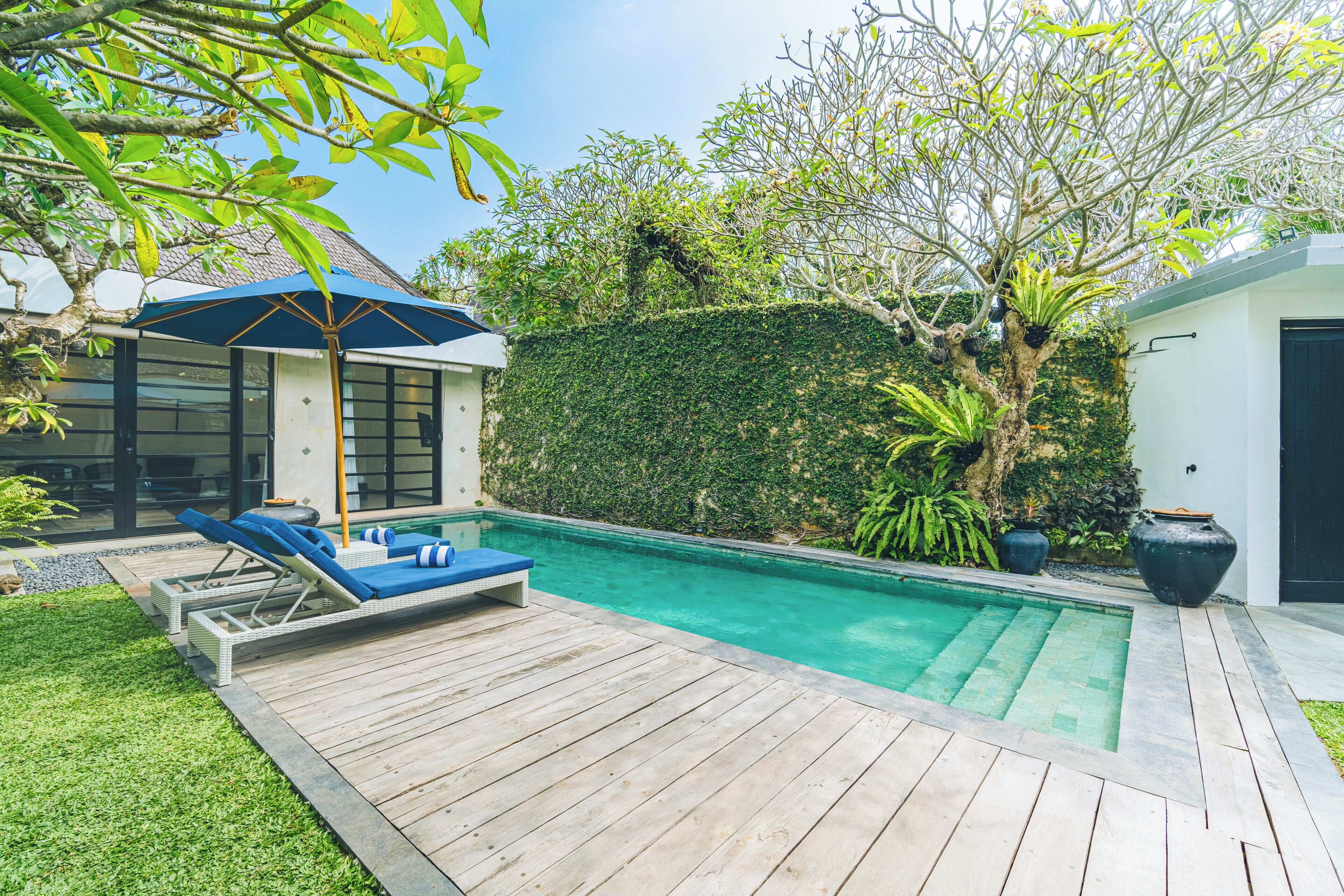 A swimming pool with a wooden deck, lounge chairs, and a covered seating area.